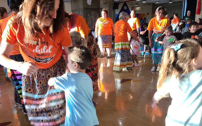 A staff member in an Every Child Matters shirt dancing with a young boy.