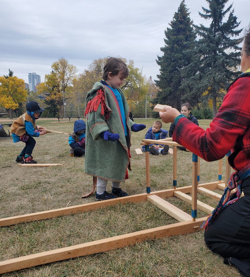 A child wearing a green capote with a woven sash, outdoors on a fall day.