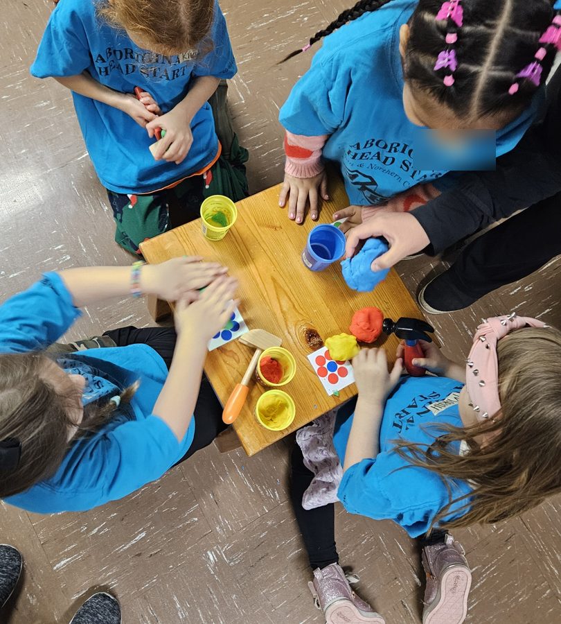 Four children shaping coloured playdough together at a low wooden table.