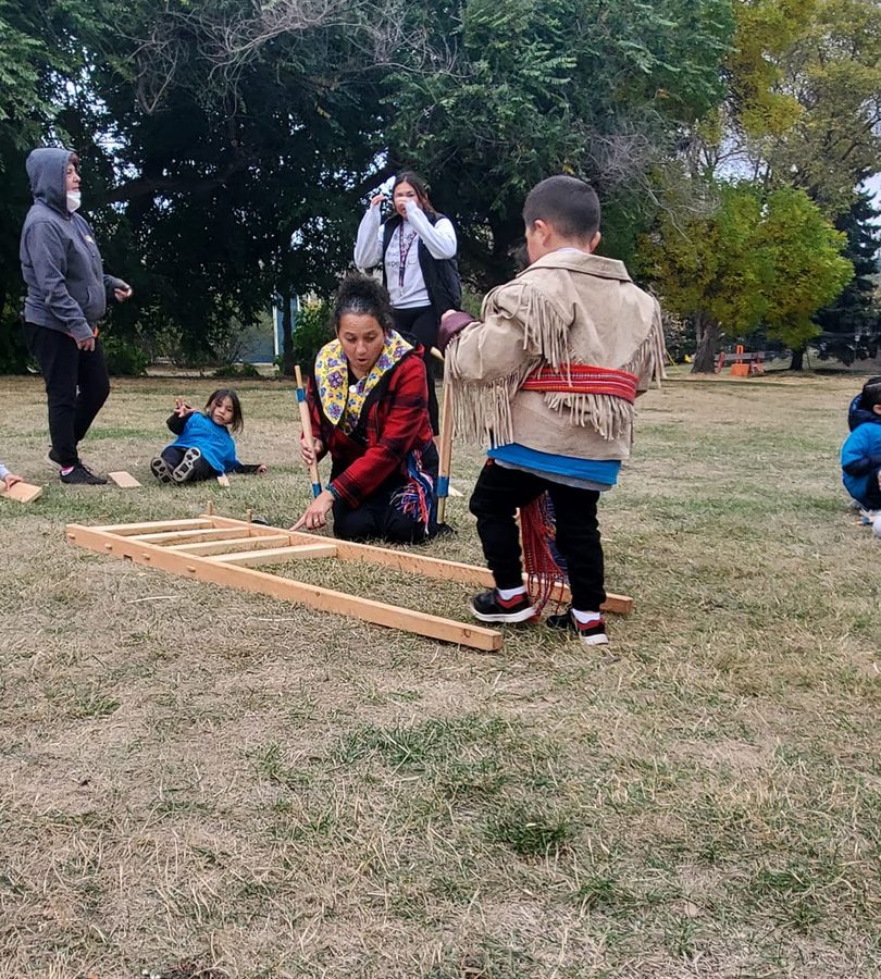Children and staff laying out wooden poles on the grass to raise a frame.
